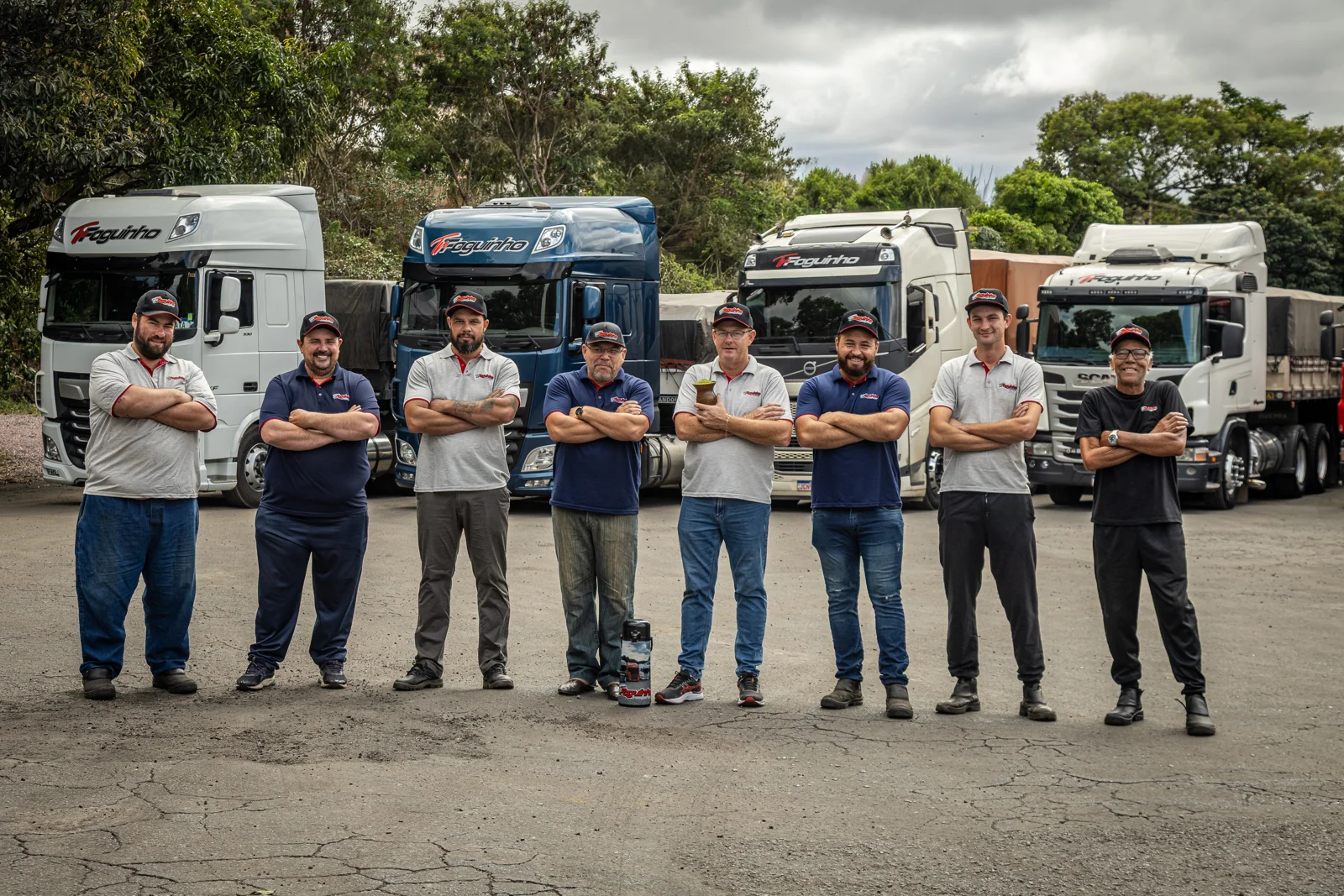 Equipe da Foguinho de braços cruzados diante de caminhões da frota no pátio